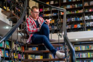 a-man-in-glasses-sits-on-the-stairs-in-the-library-for an article by kelley way titled how to deal with fanfiction