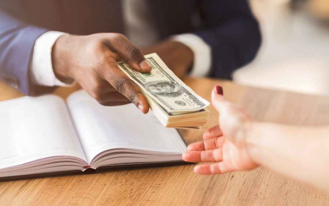man's hand holds money and is handing it to the open hand of a woman over a book for article by kelley way about Valuing Copyrights in an Estate