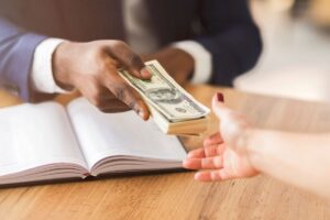 man's hand holds money and is handing it to the open hand of a woman over a book for article by kelley way about Valuing Copyrights in an Estate